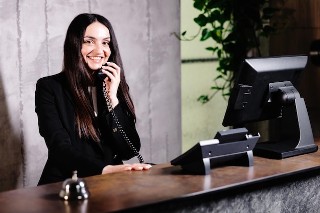 Foto recepcionista de hotel mesa de recepción de hotel moderna con campana trabajadora de recepción femenina feliz de pie en el mostrador del hotel y hablando por teléfono