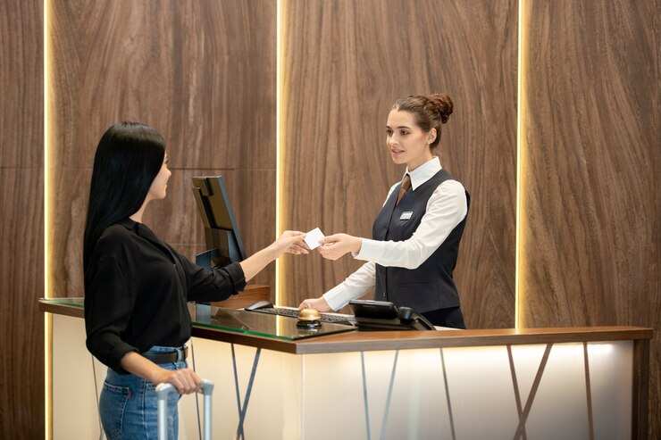 Foto recepcionista jovem morena de uniforme em pé no local de trabalho e passando o cartão plástico para um dos hóspedes no balcão da recepção no saguão do hotel