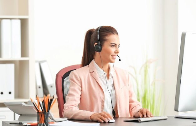 Recepcionista de sexo femenino joven que lleva puestos los auriculares en la oficina