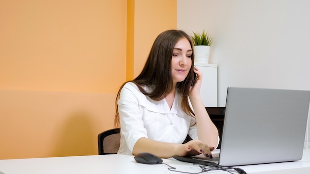 Recepcionista sorridente falando no smartphone no laptop