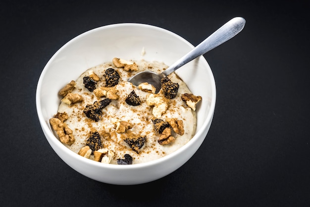 Receta de avena con nueces, ciruelas, canela y azúcar preparada para el desayuno con una cuchara sobre negro