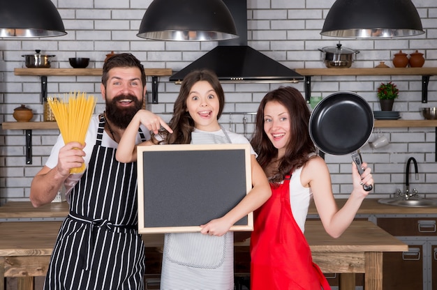 Receta de cena familiar perfecta. Madre y padre con niña sosteniendo espacio de copia de pizarra. Niña con padres cocinando. Dia familiar. Familia feliz en la cocina. Un tiempo agradable juntos.