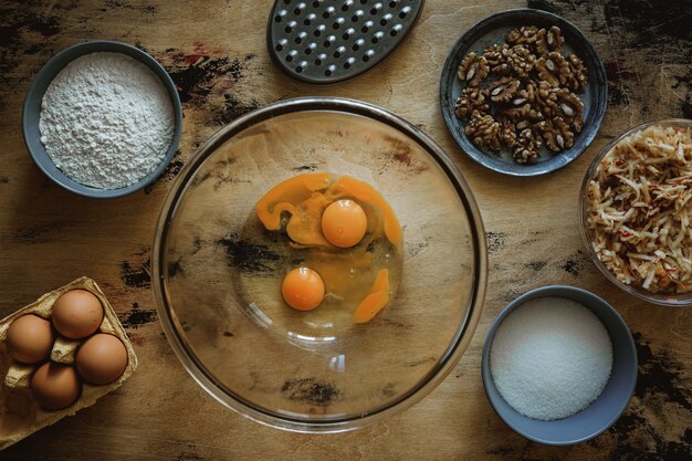 Receta de pastel de manzana, zanahoria y nueces. Huevos en un bol. Ingredientes en la mesa de madera. Harina, azúcar, huevos. Rallador.