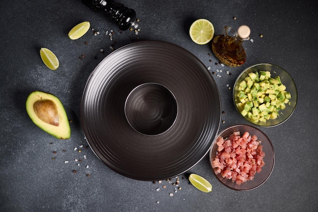 Foto receta de tartare de atún y aguacate en rodajas de ingredientes picados y en forma en una mesa oscura