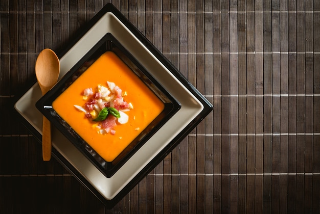 Receta típica española de salmorejo cordobés en un plato cuadrado sobre una mesa de madera