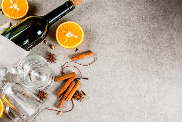 Recetas de bebidas calientes de Navidad, conjunto de ingredientes para vino caliente: botella de vino, vasos de vidrio, especias, naranja. Fondo de piedra gris, vista superior de copyspace