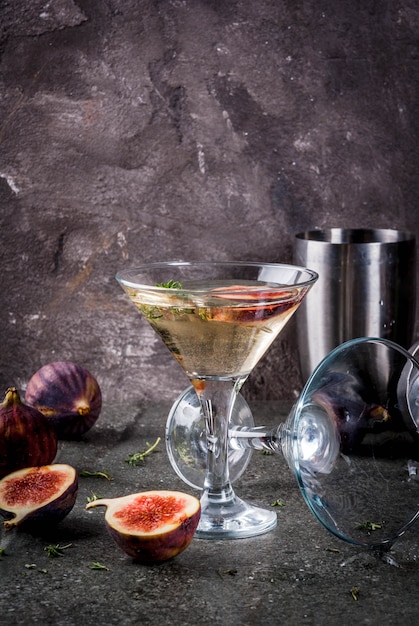 Recetas de bebidas de otoño e invierno, cóctel de Martini con higos, tomillo y miel, sobre mesa de piedra negra,