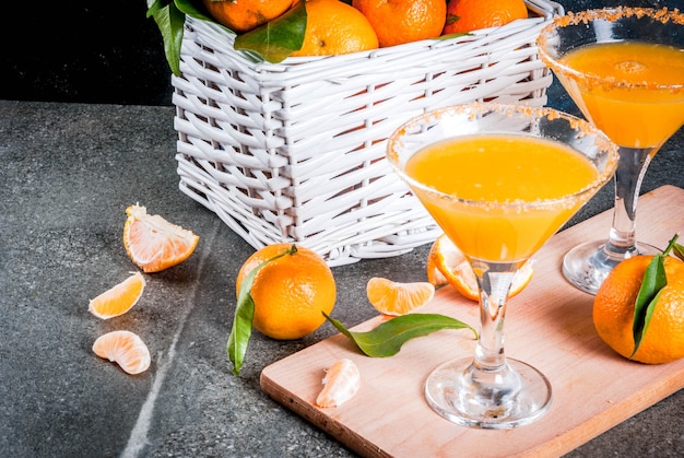 Recetas e ideas de cócteles de frutas de invierno, mandarina martini margarita con mandarinas frescas en la cesta, sobre fondo oscuro, espacio de copia