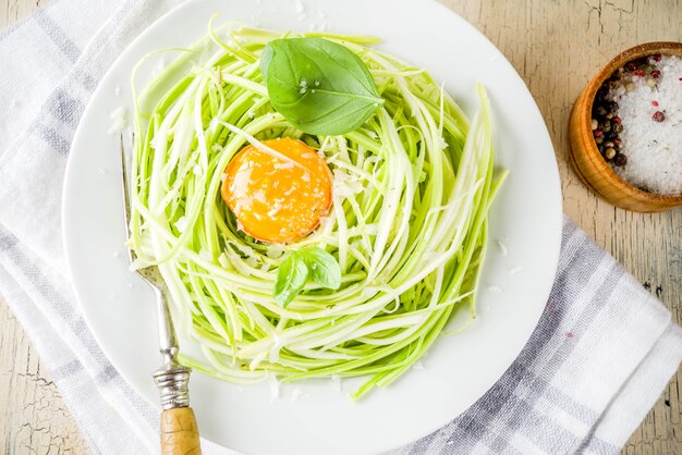 Recetas veganas de moda, pasta de espagueti con calabacín y queso con yema de huevo con parmesano, aceite de oliva y hojas de albahaca, superficie de hormigón ligero