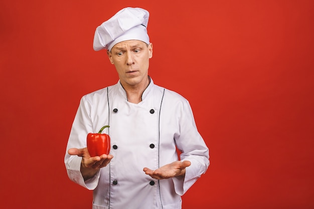 Recetas De Verduras. Cocinero sonriente Man Holding Red Sweet Pepper que cocina la comida que se coloca sobre fondo rojo aislado del estudio.