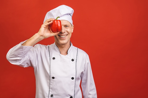 Recetas De Verduras. Cocinero sonriente Man Holding Red Sweet Pepper que cocina la comida que se coloca sobre fondo rojo aislado del estudio.