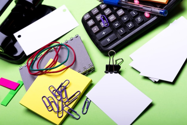 Rechner und Schreibwaren Office-Tools auf grünem Hintergrund Nahaufnahme Notebook in grauer Farbe Locher Visitenkarten Haftnotizen Gummibänder und Clips Geschäfts- und Büroarbeitskonzept