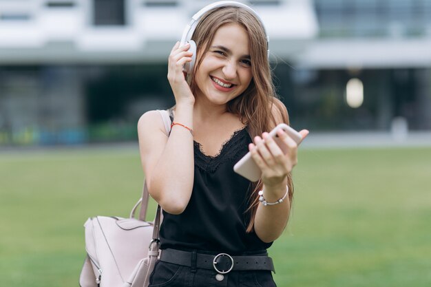 Recht attraktives Jugendstudentenmädchen hört Musik vom Telefon in den Kopfhörern