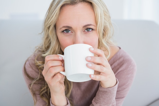 Recht blond auf der Couch, die heißes Getränk trinkt