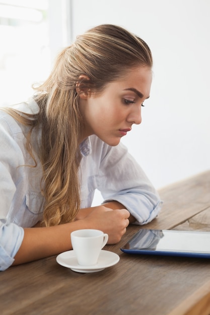 Recht blond, einen Kaffee unter Verwendung des Tabletten-PC trinkend