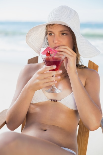 Recht blond, entspannend im Klappstuhl auf dem Strand mit Cocktail