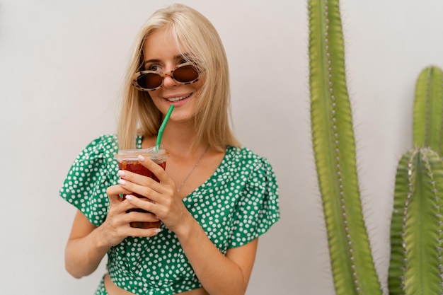 Recht blonde Frau im stilvollen Frühlingskleid, das leckere Limonade hält und über weißem Hintergrund aufwirft