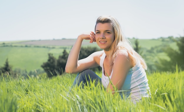 Recht blondes Lächeln an der Kamera, die auf Gras sitzt