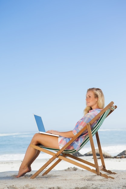 Recht blondes Sitzen auf Strand unter Verwendung ihres Laptops