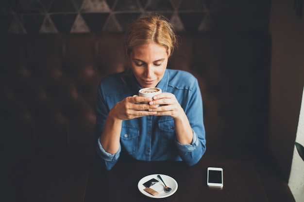 Recht junge blonde Frau, die im Café sitzt