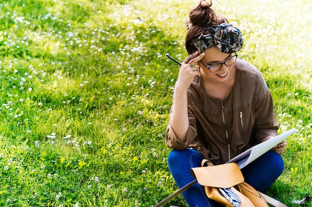 Recht junge Frau, die draußen auf dem Gras und dem Lesebuch sitzt