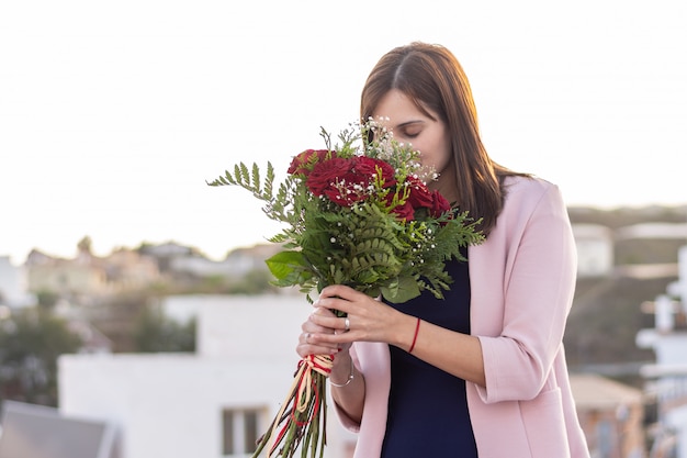 Recht junge Frau, die ihren Blumenstrauß der roten Rosen riecht.