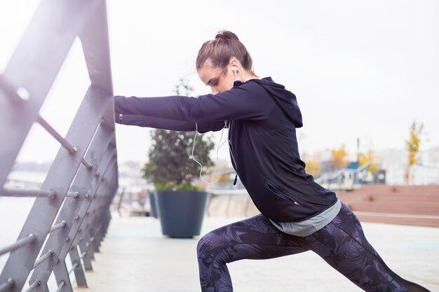 Recht junge Frau mit den Kopfhörern, die während des Sporttrainings ausdehnen