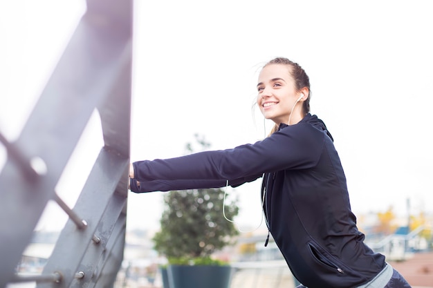 Recht junge Frau mit den Kopfhörern, die während des Sporttrainings ausdehnen