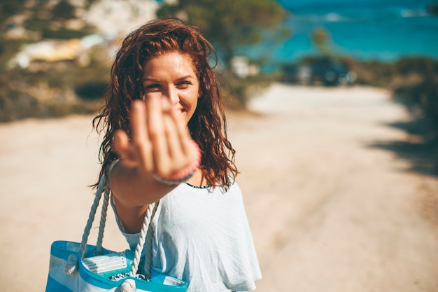 Recht junge Frau mit einer Tasche auf dem Strand am sonnigen Sommertag