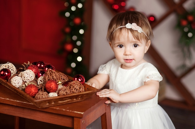 Recht kleines Mädchen im weißen Kleid, das über Weihnachtslichter spielt und glücklich ist