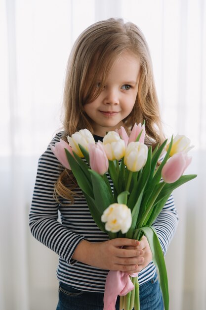 Recht kleines Mädchen mit Bündel Tulpen an einem glücklichen Mutter-Tag. Macht ein Geschenk für ihre Mutter.