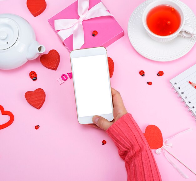 Rechte weibliche Hand in einer rosa Strickjacke hält einen weißen Smartphone