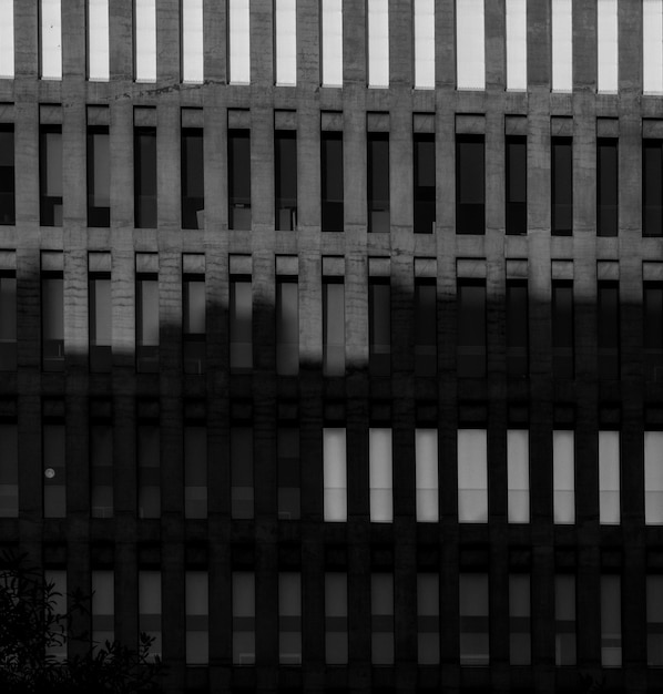 Rechteckige Fenster eines modernen Gebäudes in der Stadt der Justiz unter einem Sonnenuntergangslicht und Schatten eines anderen Gebäudes in Schwarz und Weiß