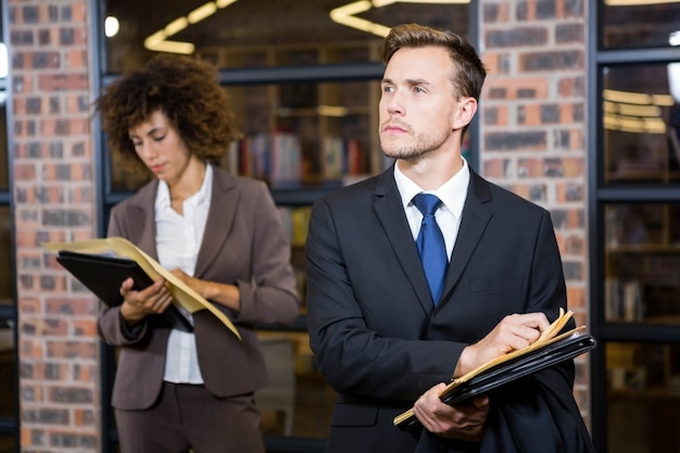 Rechtsanwalt, der nahe Bibliothek steht und Dokumente betrachtet