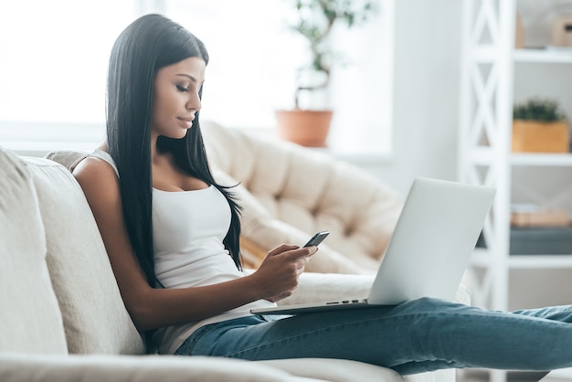 Recibir mensajes. Mujer joven atractiva que mira el teléfono móvil mientras se relaja en el sofá en casa