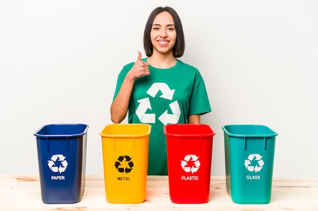 Reciclagem de jovem hispânica isolada no fundo branco sorrindo e levantando o polegar