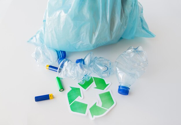 reciclagem de resíduos, reutilização, eliminação de lixo, meio ambiente e conceito de ecologia - close-up de garrafas de água de plástico usadas e baterias com saco de lixo e símbolo de reciclagem verde
