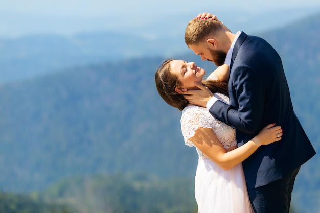 Recién casados abrazándose con ropa festiva la novia ha cerrado los ojos y el novio la mira con una mirada amable