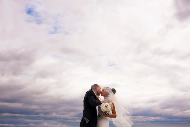 Los recién casados se besan en la nube en el muelle del mar