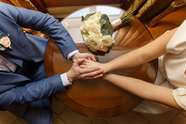 Recién casados cogidos de la mano cerca de ramo de boda