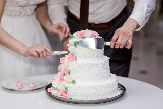 Recién casados cortan pastel festivo de varios pisos en tono blanco