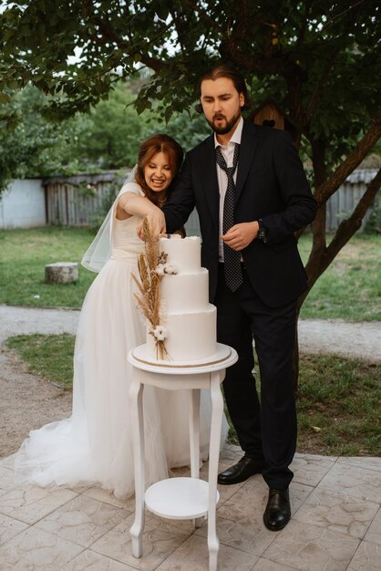 Los recién casados cortan y prueban felizmente el pastel de bodas