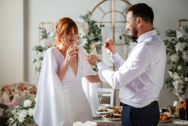 Los recién casados cortan y prueban felizmente el pastel de bodas