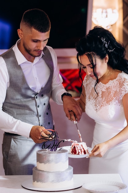 Los recién casados cortan y prueban felizmente el pastel de bodas