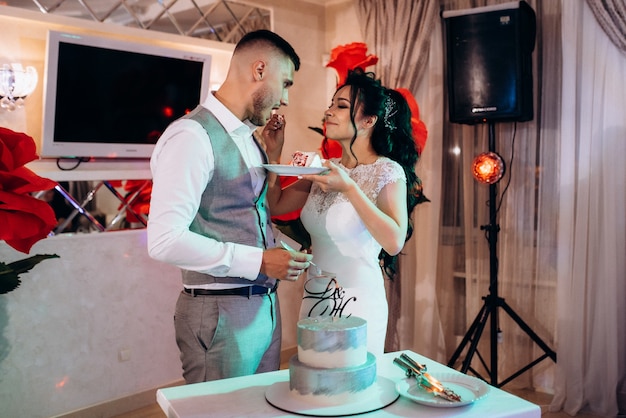 Los recién casados cortan y prueban felizmente el pastel de bodas