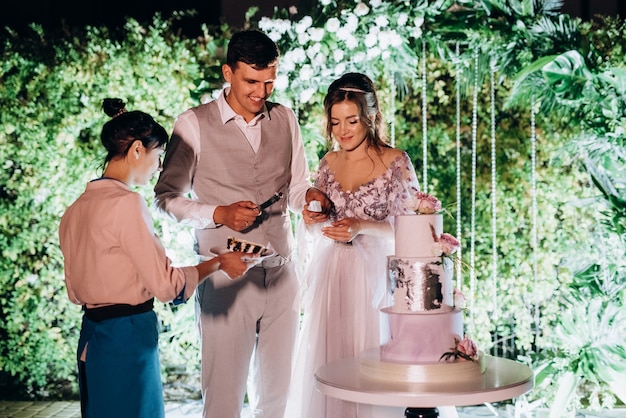 Los recién casados cortan y prueban felizmente el pastel de bodas