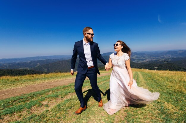 Los recién casados se dan la mano y caminan por la cima de la montaña.