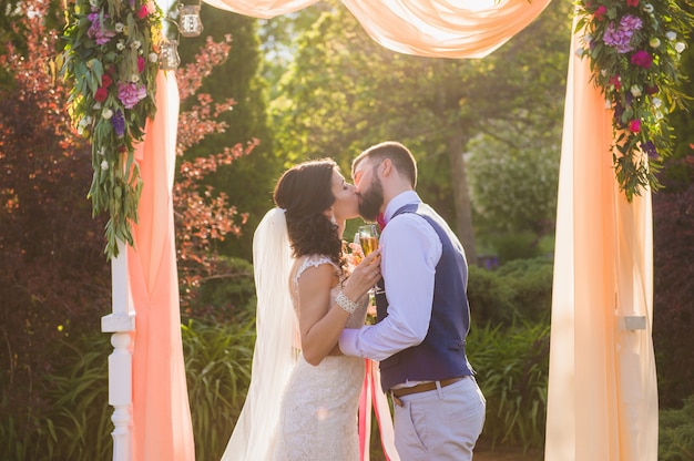 Recién casados enamorados bajo el arco al aire libre