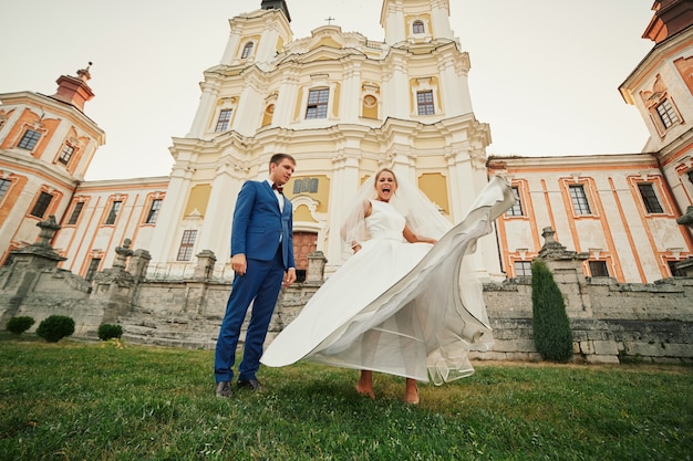 Recién casados felices y divertidos posando en el patio cerca de la iglesia