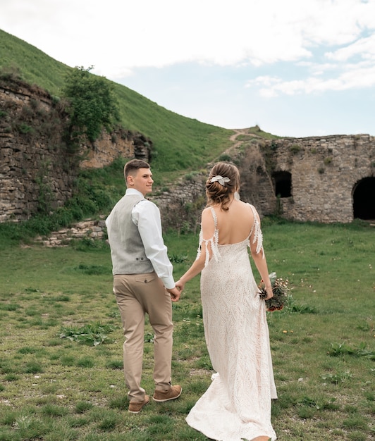 Los recién casados felices están tomados de la mano en el fondo del castillo